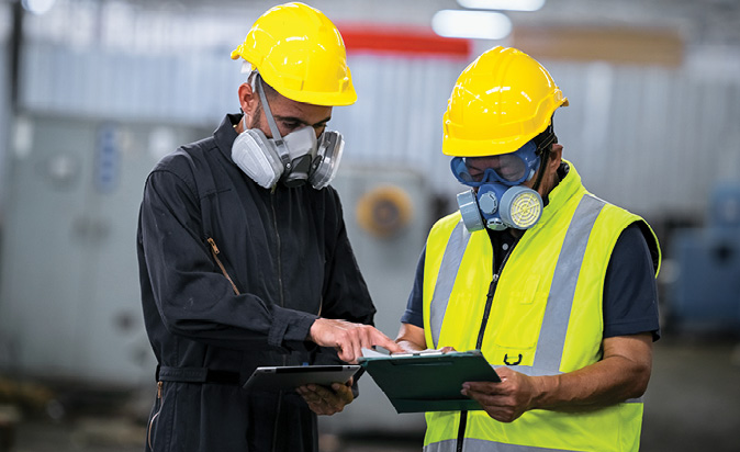 Health and safety officer in protective clothing with clipboard instructs workers